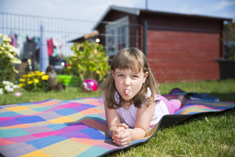 Porträt eines kleinen Mädchens, das auf einer Decke liegt und die Zunge herausstreckt, lizenzfreies Stockfoto
