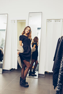 Lächelnde junge Frau präsentiert neue Kleidung in einer Boutique - CHAF001328
