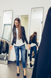 Lächelnde junge Frau präsentiert neue Kleidung in einer Boutique - CHAF001330