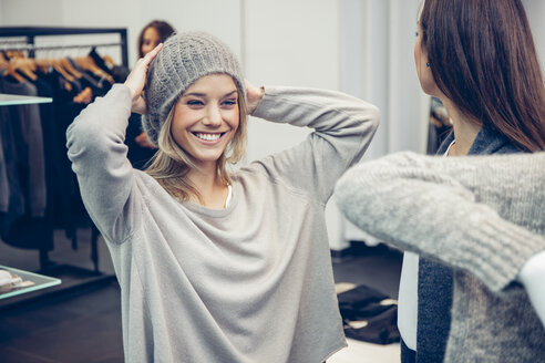 Happy oung woman putting on woolly hat in a boutique - CHAF001348