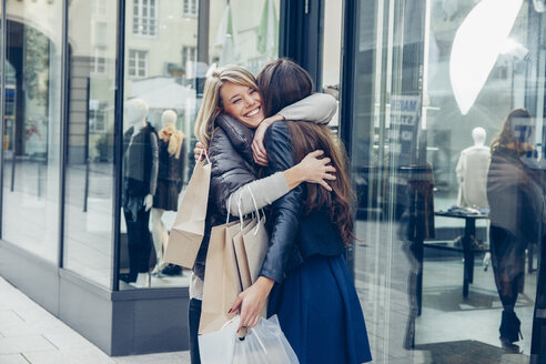Zwei glückliche junge Frauen mit Einkaufstaschen umarmen sich vor einem Geschäft - CHAF001354