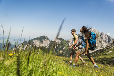 Österreich, Tirol, Tannheimer Tal, junges Paar wandert auf Almwiese - UUF005050
