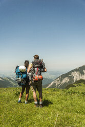 Österreich, Tirol, Tannheimer Tal, junges Paar steht auf einer Almwiese und betrachtet die Aussicht - UUF005056