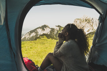 Österreich, Tirol, Tannheimer Tal, junge Frau sitzt im Zelt auf einer Almwiese - UUF005131