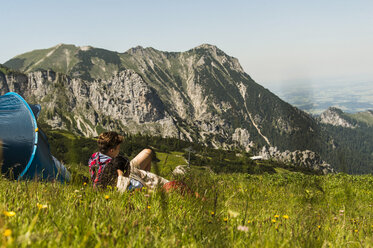 Österreich, Tirol, Tannheimer Tal, junges Paar ruht sich auf einer Almwiese neben dem Zelt aus - UUF005062