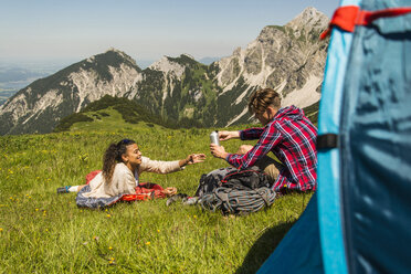 Österreich, Tirol, Tannheimer Tal, junges Paar ruht sich auf einer Almwiese neben dem Zelt aus - UUF005063