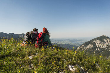 Austria, Tyrol, Tannheimer Tal, young couple sitting on alpine meadow looking at view - UUF005095