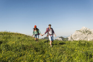 Österreich, Tirol, Tannheimer Tal, junges Paar spaziert Hand in Hand über eine Almwiese - UUF005105