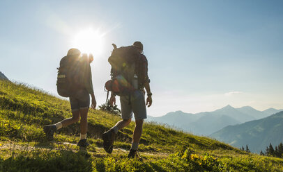 Österreich, Tirol, Tannheimer Tal, junges Paar wandert auf Almwiese im Gegenlicht - UUF005109