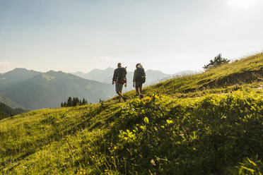 Austria, Tyrol, Tannheimer Tal, young couple hiking on alpine meadow in backlight - UUF005110