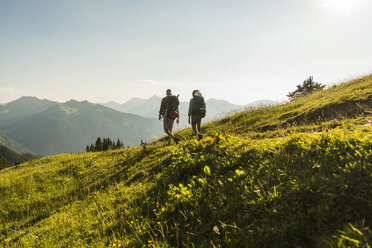 Österreich, Tirol, Tannheimer Tal, junges Paar wandert auf Almwiese im Gegenlicht - UUF005110