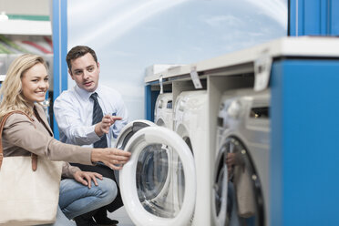 Shop assistant explaining washing machine to customer - ZEF007072