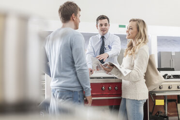 Shop assistant talking to young couple shopping kitchen equipment - ZEF007082