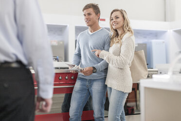 Young couple shopping kitchen equipment looking at shop assistant - ZEF007083