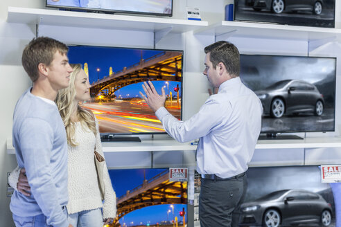 Verkäufer zeigt einem jungen Paar Flachbildfernseher - ZEF007472
