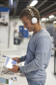 Junge Frau mit Kopfhörern testet digitales Tablet in einem Geschäft - ZEF007361