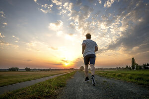 Rückansicht eines joggenden Mannes bei Sonnenuntergang - PUF000392