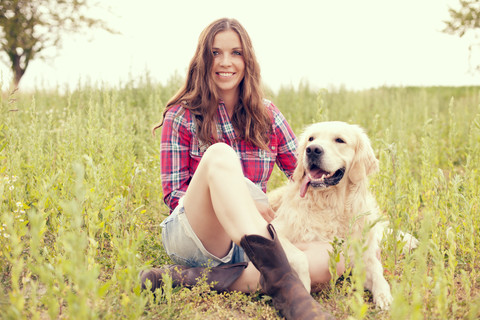 Frau und ihr Golden Retriever sitzen auf einer Wiese, lizenzfreies Stockfoto