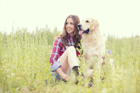 Frau und ihr Golden Retriever sitzen auf einer Wiese, lizenzfreies Stockfoto