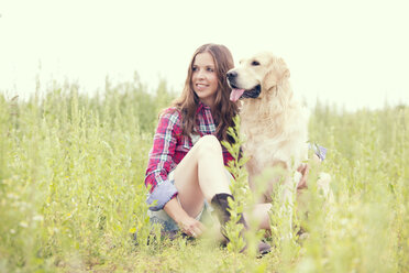 Woman and her Golden Retriever sitting on a meadow - MAEF010820