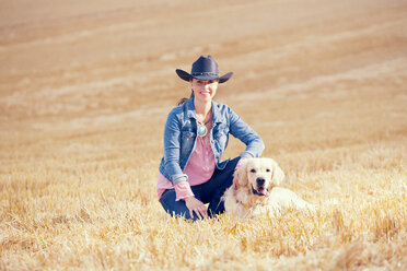 Portrait of young woman sitting with Golden Retriever on a stubble field - MAEF010819