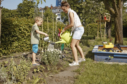 Mutter und Sohn gießen Blumen im Garten, lizenzfreies Stockfoto