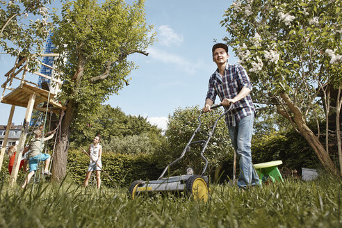 Mann mäht Rasen im Garten mit Familie im Hintergrund - RHF001030