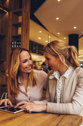 Two female friends with digital tablet communicating in a coffee shop - CHAF001031