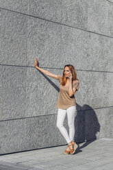 Young woman leaning on a wall talking on mobile phone - CHAF001034