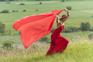Woman in red dress running on a meadow with red cloth - TCF004766