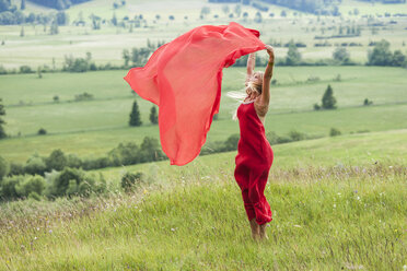 Woman in red dress standing on a meadow holding red cloth - TCF004767