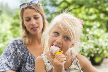 Girl eating popsicle with mother in background - TCF004770