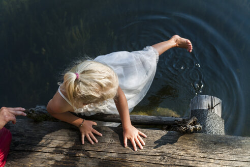 Girl in summer dress with foot in a lake - TCF004781