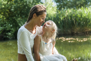 Girl kissing mother at a lake - TCF004786