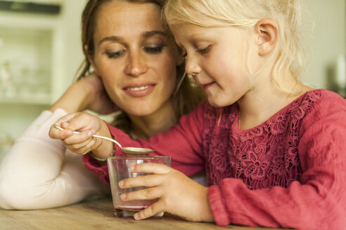 Mother looking at daughter with glass and spoon - TCF004795