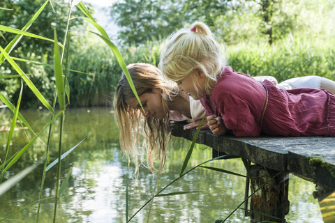 Mutter und Tochter liegen auf einem Steg an einem See und schauen aufs Wasser, lizenzfreies Stockfoto