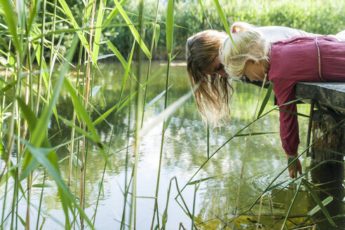 Mother and daughter lying on jetty at a lake looking at water - TCF004800