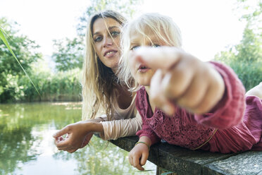 Girl lying with mother on jetty at a lake pointing finger - TCF004802
