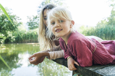 Mutter und lächelnde Tochter liegen auf einem Steg an einem See - TCF004803