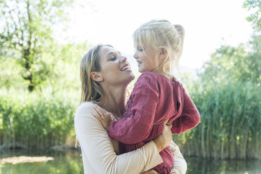 Mother holding daughter at a lake - TCF004807