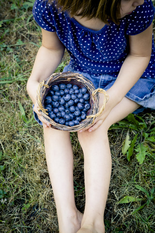 Kleines Mädchen auf einer Wiese sitzend mit Weidenkorb voller Blaubeeren, lizenzfreies Stockfoto