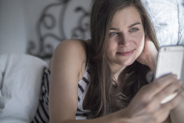 Junge Frau liegt im Bett und macht ein Selfie mit ihrem Smartphone - RIBF000165