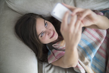 Junge Frau entspannt sich auf der Couch und macht ein Selfie mit ihrem Smartphone - RIBF000172