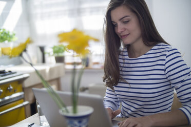 Junge Frau mit Laptop, die von zu Hause aus arbeitet - RIBF000179