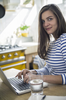 Junge Frau mit Laptop, die von zu Hause aus arbeitet - RIBF000241