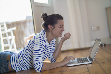 Young woman at home lying on wooden floor, using laptop - RIBF000181