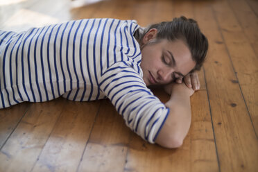 Young woman at home lying on wooden floor, eyes closed - RIBF000184
