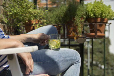 Junge Frau sitzt auf dem Balkon und trinkt Tee - RIBF000185