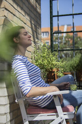 Young woman sitting on balcony, drinking tea, eyes closed - RIBF000186