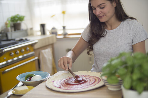 Junge Frau, die Tomatensauce auf Pizzateig verteilt - RIBF000196